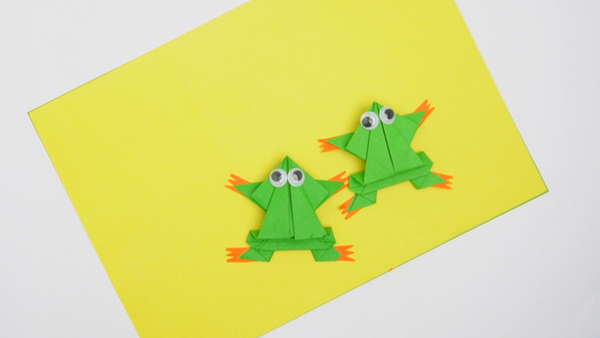 Finished jumping paper frog craft featuring a green folded paper frog with a compact body, raised eyes, and folded legs for jumping.