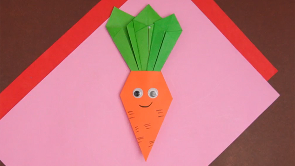 Finished paper carrot craft featuring an orange carrot shape with a pointed bottom and green paper leaves on top.